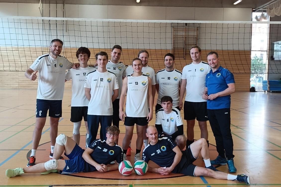 Gruppe von elf Volleyballspielern in Sportkleidung, posierend in einer Halle mit Volleyballnetz im Hintergrund.