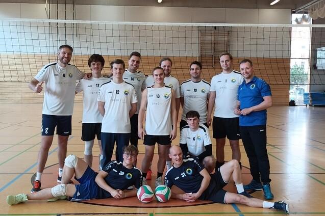 Gruppe von elf Volleyballspielern in Sportkleidung, posierend in einer Halle mit Volleyballnetz im Hintergrund.