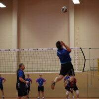 Spieler springt hoch in der Luft und schlägt einen Volleyball während eines Spiels in einer Sporthalle.