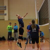 Spieler springt zum Volleyball-Angriff, während Teamkameraden auf dem Spielfeld zuschauen.