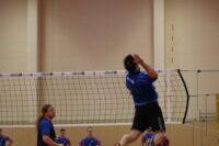Spieler springt hoch in der Luft und schlägt einen Volleyball während eines Spiels in einer Sporthalle.