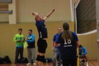Spieler springt zum Volleyball-Angriff, während Teamkameraden auf dem Spielfeld zuschauen.