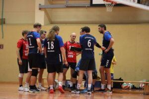 Eine Gruppe von Handballspielern berät sich während einer Spielpause in einer Sporthalle.