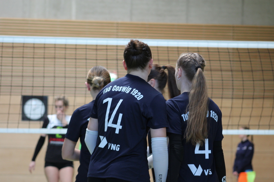 Drei Volleyballspielerinnen in blauen Trikots stehen am Netz, eine Spielerin mit der Nummer 14 ist im Vordergrund.