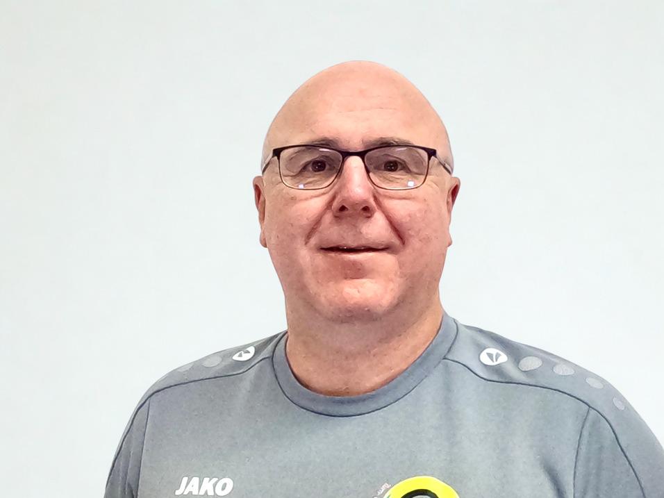 Portrait eines schädelglatten Mannes mit Brille, in grauem Sportshirt, vor einem hellen Hintergrund.
