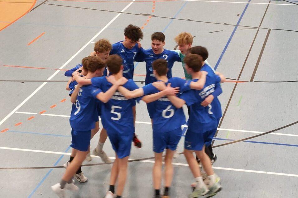 Zehn Jugendliche in blauen Trikots umarmen sich in einer Sporthalle und feiern ein Team-Moment.