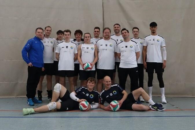 Gruppenfoto einer Volleyballmannschaft mit 15 Spielern in weißen und schwarzen Trikots, einige halten Volleybälle.