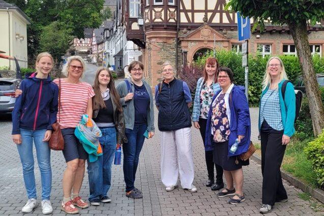 Gruppe von sieben Frauen steht auf einem Fu&szlig;weg vor historischen Geb&auml;uden und einem Park in einer Stadt.