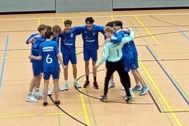 Eine Gruppe von acht jungen Sportlern in blauen Trikots umarmt sich auf einem Hallenboden, bereit f&uuml;r das Spiel.
