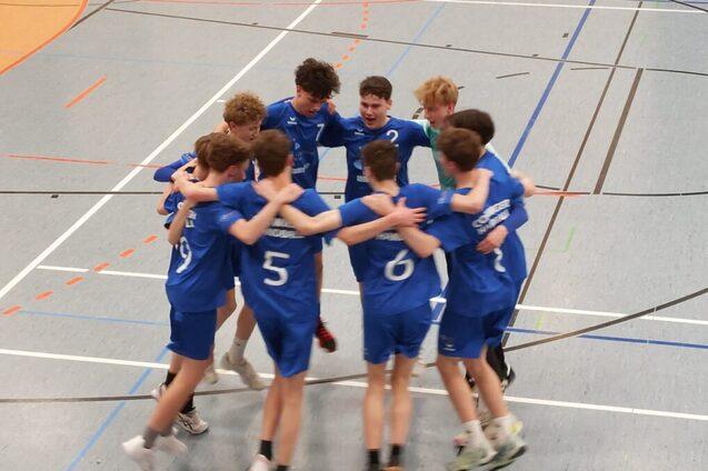 Zehn Jugendliche in blauen Trikots umarmen sich in einer Sporthalle und feiern ein Team-Moment.