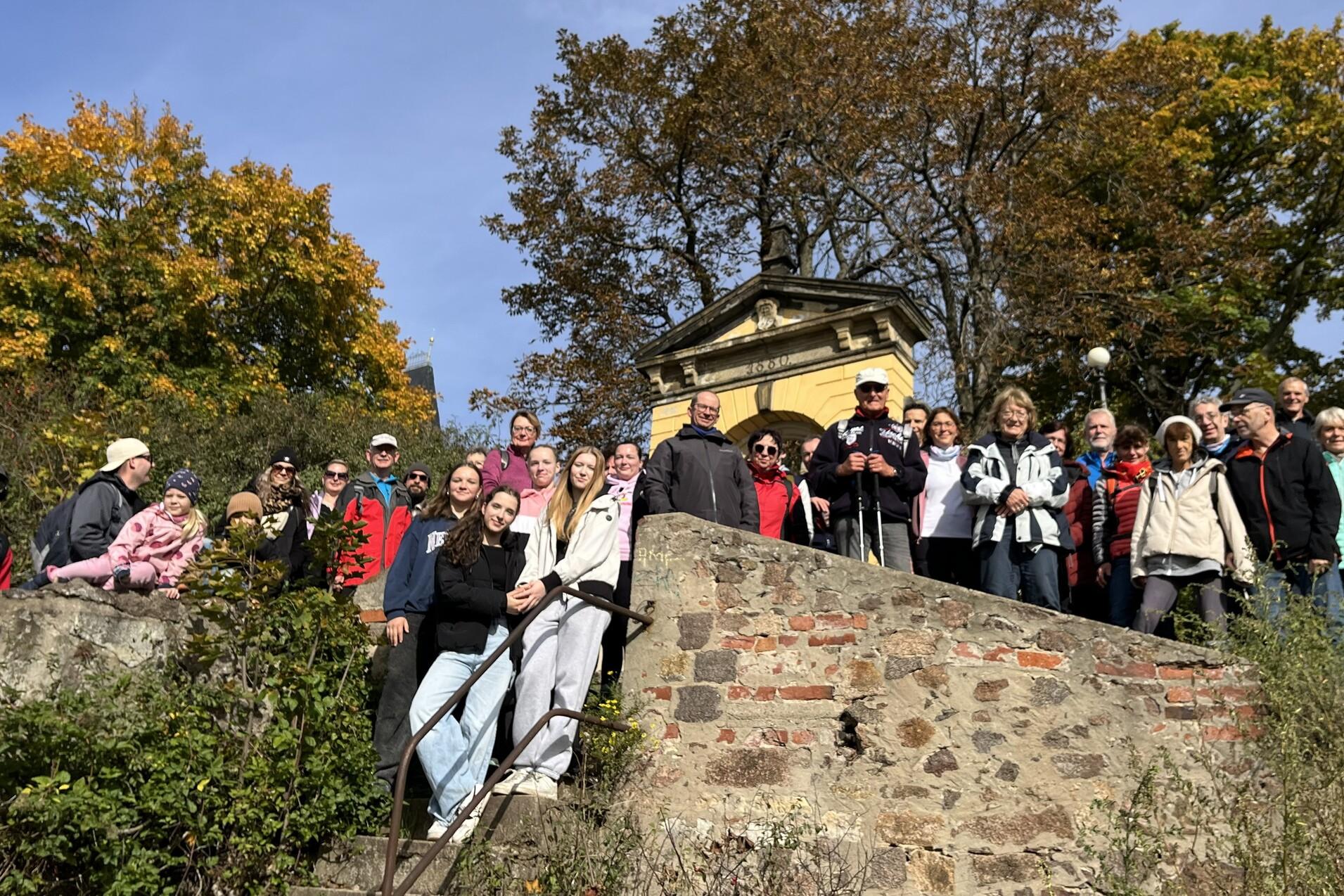 Gruppensfoto von 20 Personen auf einer Treppe vor einem historischen Gebäude, umgeben von herbstlichen Bäumen.