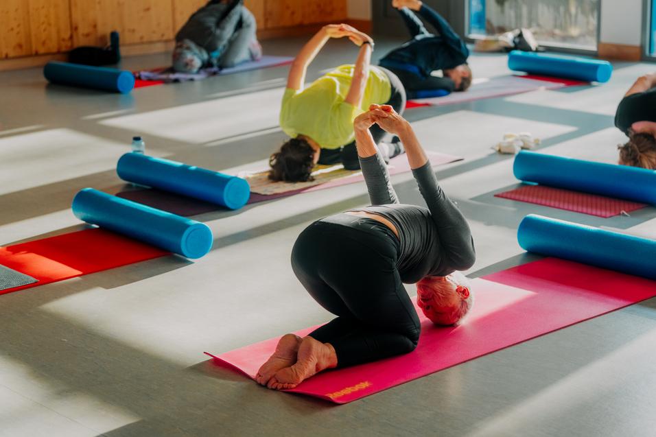 Gruppe von Menschen übt Yoga auf Matten, mit Schaumstoffrollen in einem hellen Raum.