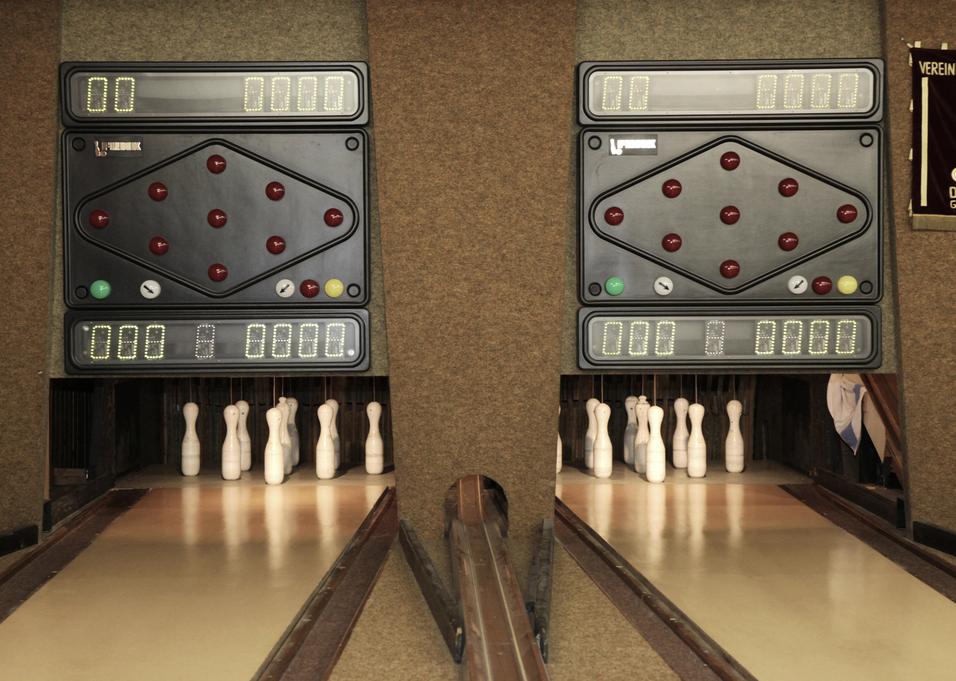 Zwei Bowlingbahnen mit Anzeigetafeln und weißen Kegel, die hinter einer Trennwand stehen.