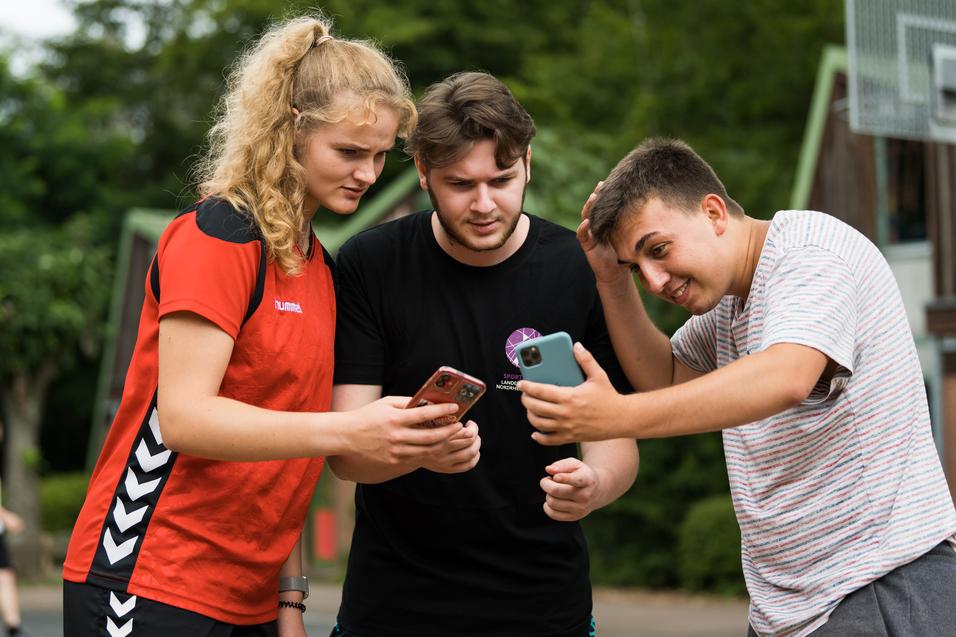 Drei Jugendliche stehen zusammen und schauen auf ihre Smartphones, um etwas anzusehen oder zu besprechen.