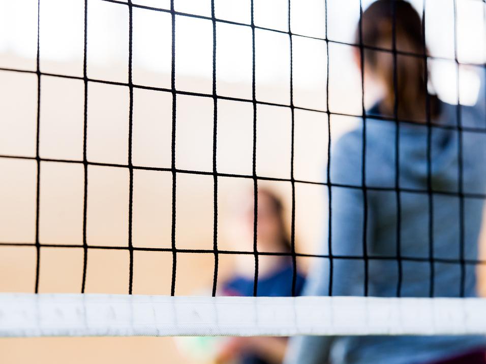 Nahaufnahme eines Volleyballnetzes mit unscharfen Spielern im Hintergrund in einer Sporthalle.